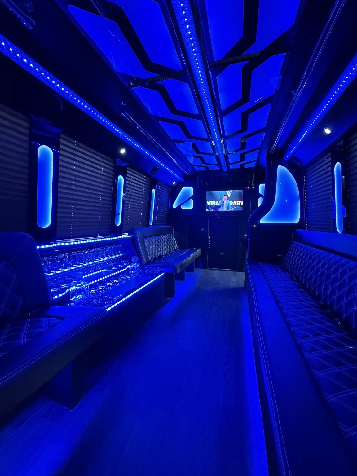 Party bus lounge with blue ceiling lights and seating along both sides